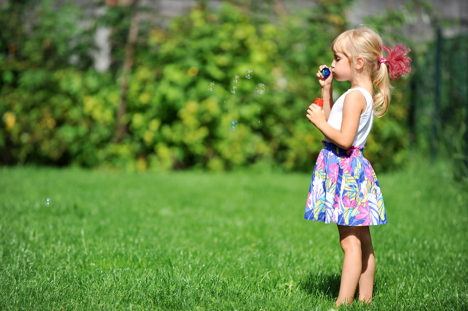 A girl blowing bubbles on a green lawn